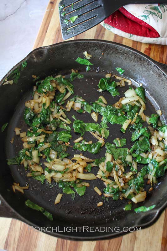 Spinach and diced onions in a cast iron skillet.