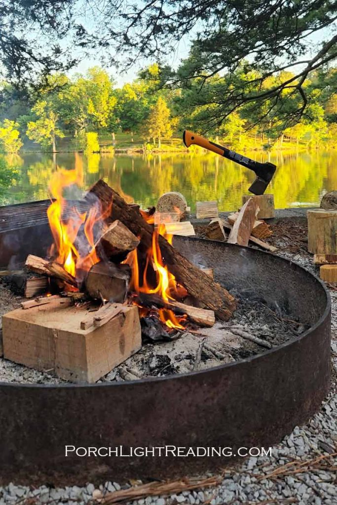 Campfire with hatchet next to a mirrored lake.