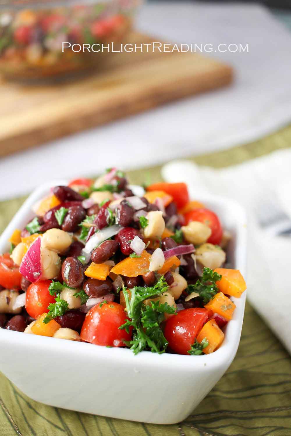 Three bean salad recipe with sliced tomatoes, fresh parsley, and bight orange peppers.