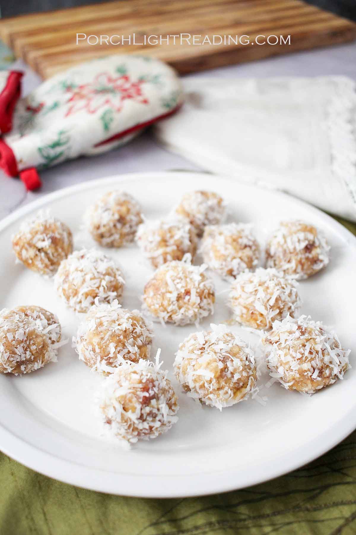 Bite size coconut date nut balls on a white plate with poinsettia oven mitts in the background.