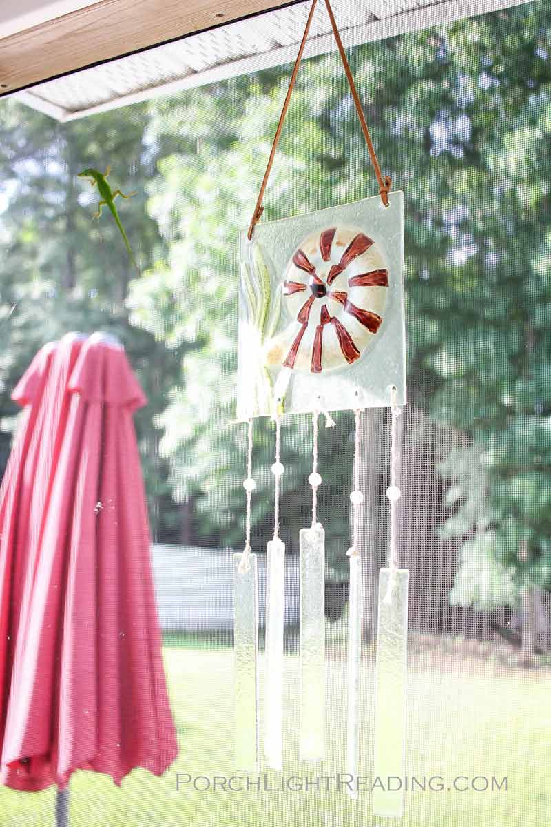 Sea glass wind chime with a bright green gecko on the screened in porch screen. 