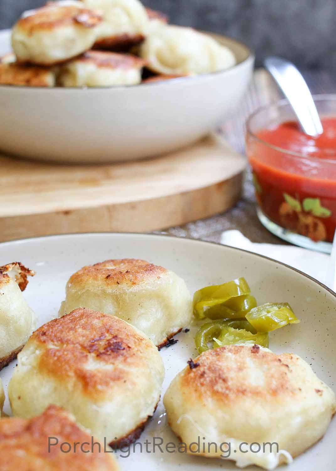 Pizza bites arranged on a plate with jalapeños and pizza sauce. 