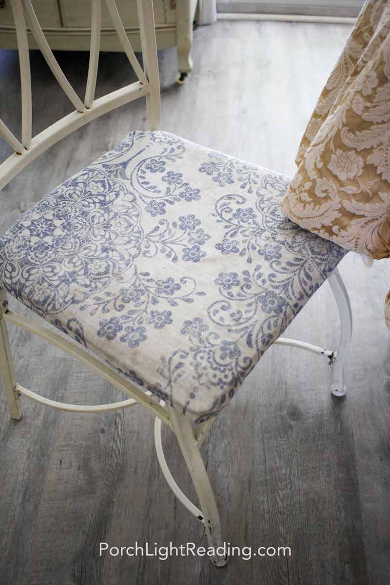 Old white metal table with faded blue chair cushion.