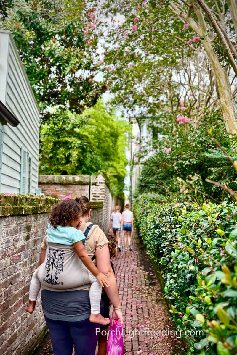 Mom carrying toddler on back in a Tula along the streets of Charleston. 