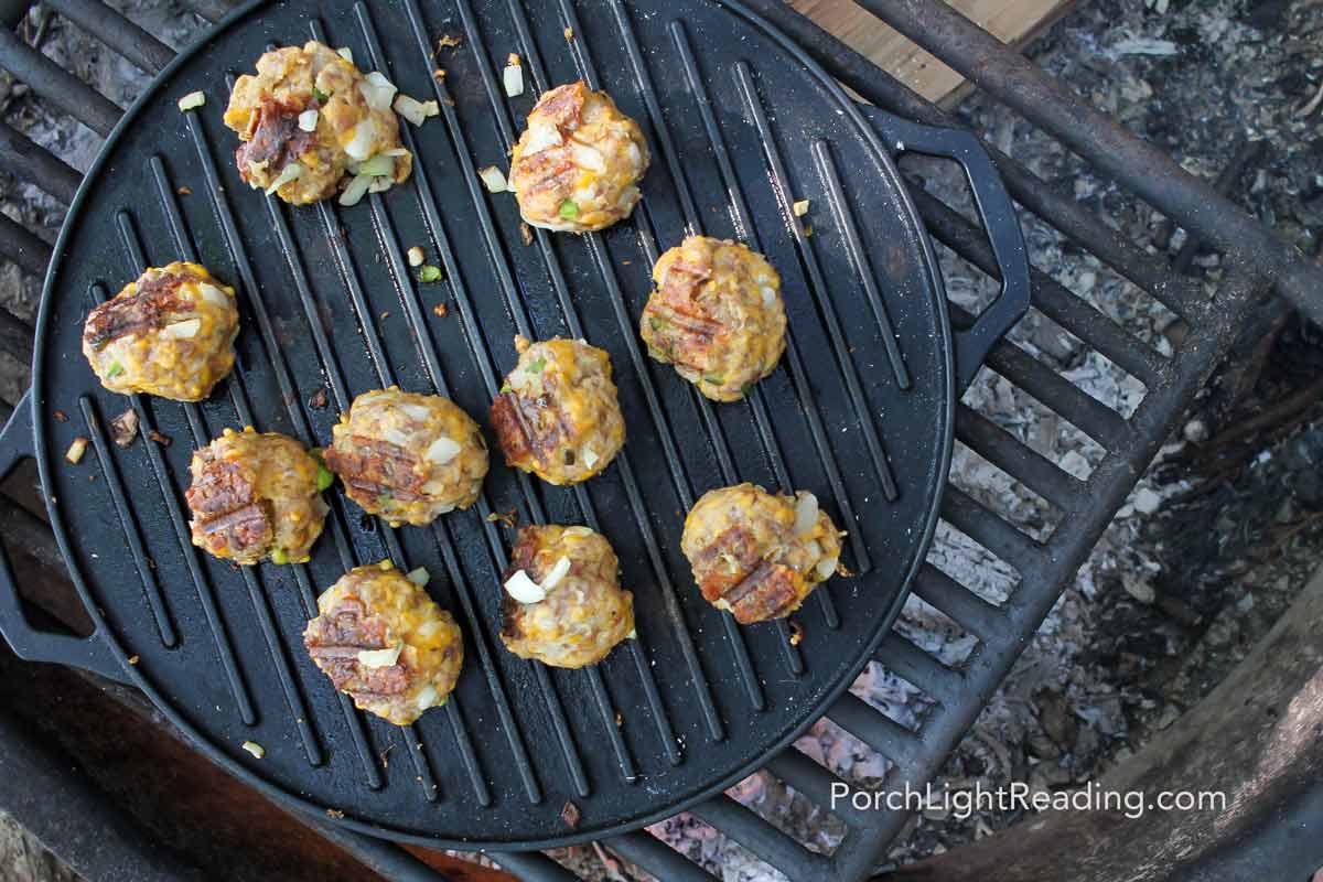 Camping breakfast sausage balls cooking over a griddle over the campfire.