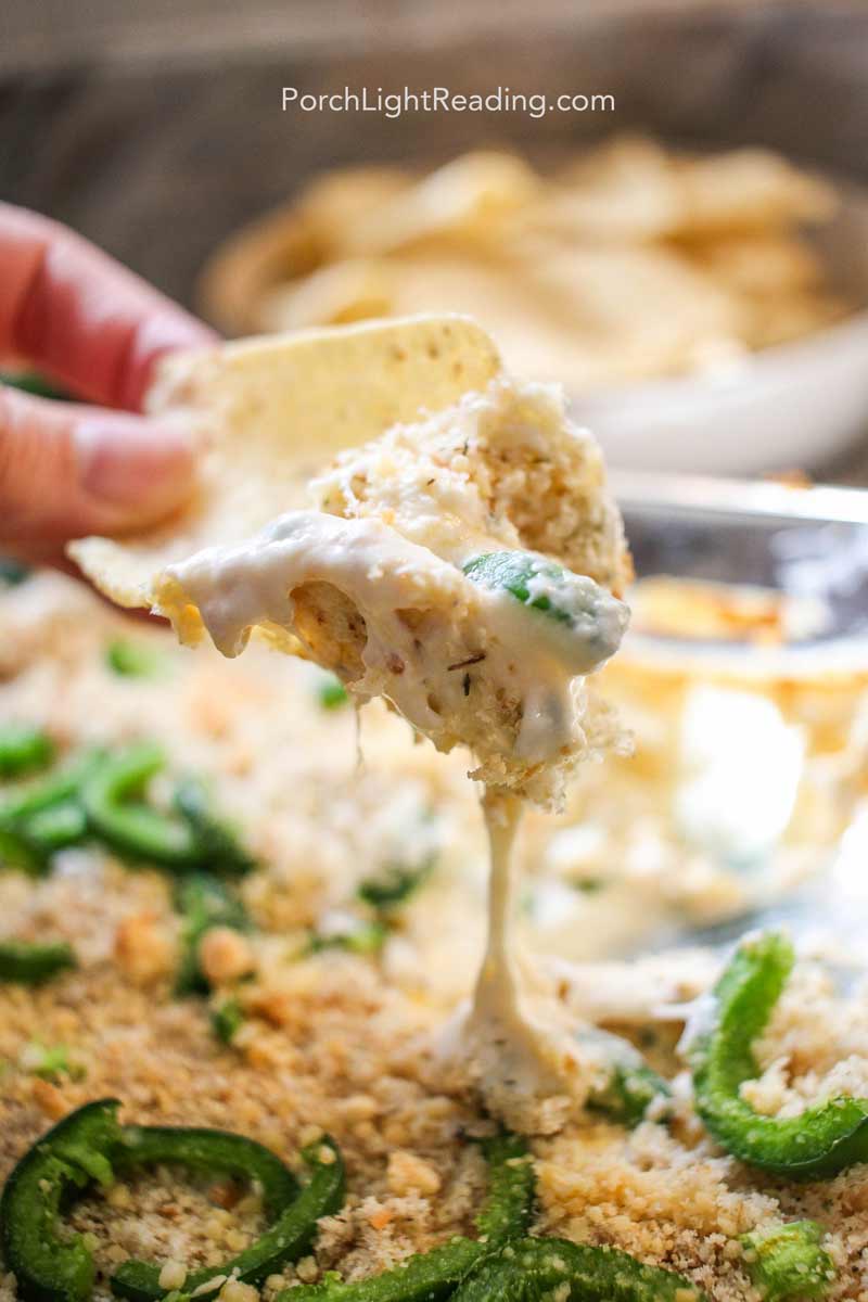 Creamy jalapeno popper dip on a tortilla chip, dripping with cheese. 