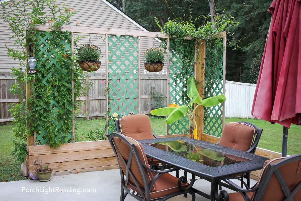 Patio with designated dinning area and trellis privacy screen with greenery. 
