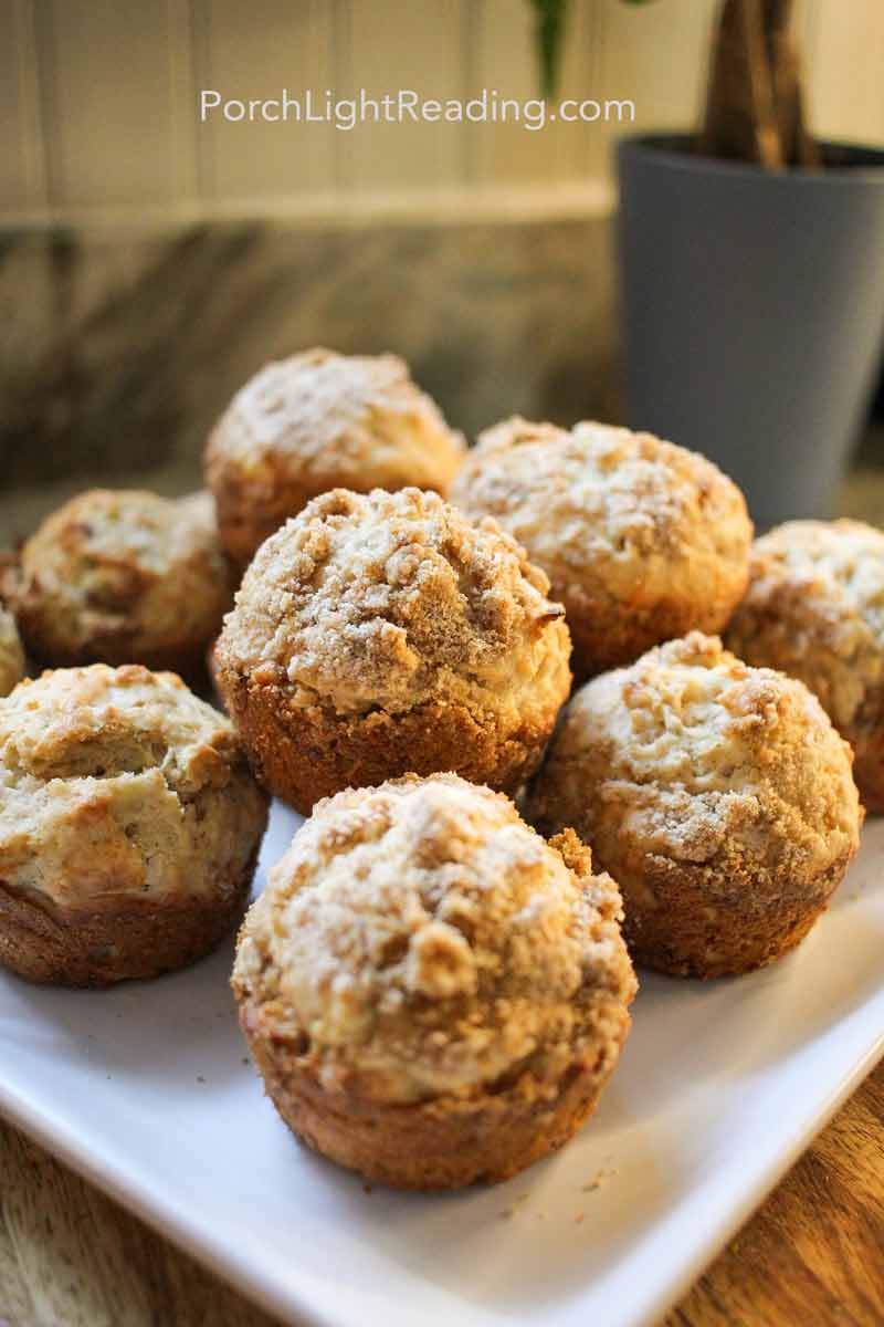 Piled apple muffins with a streusel topping on a white plate. 