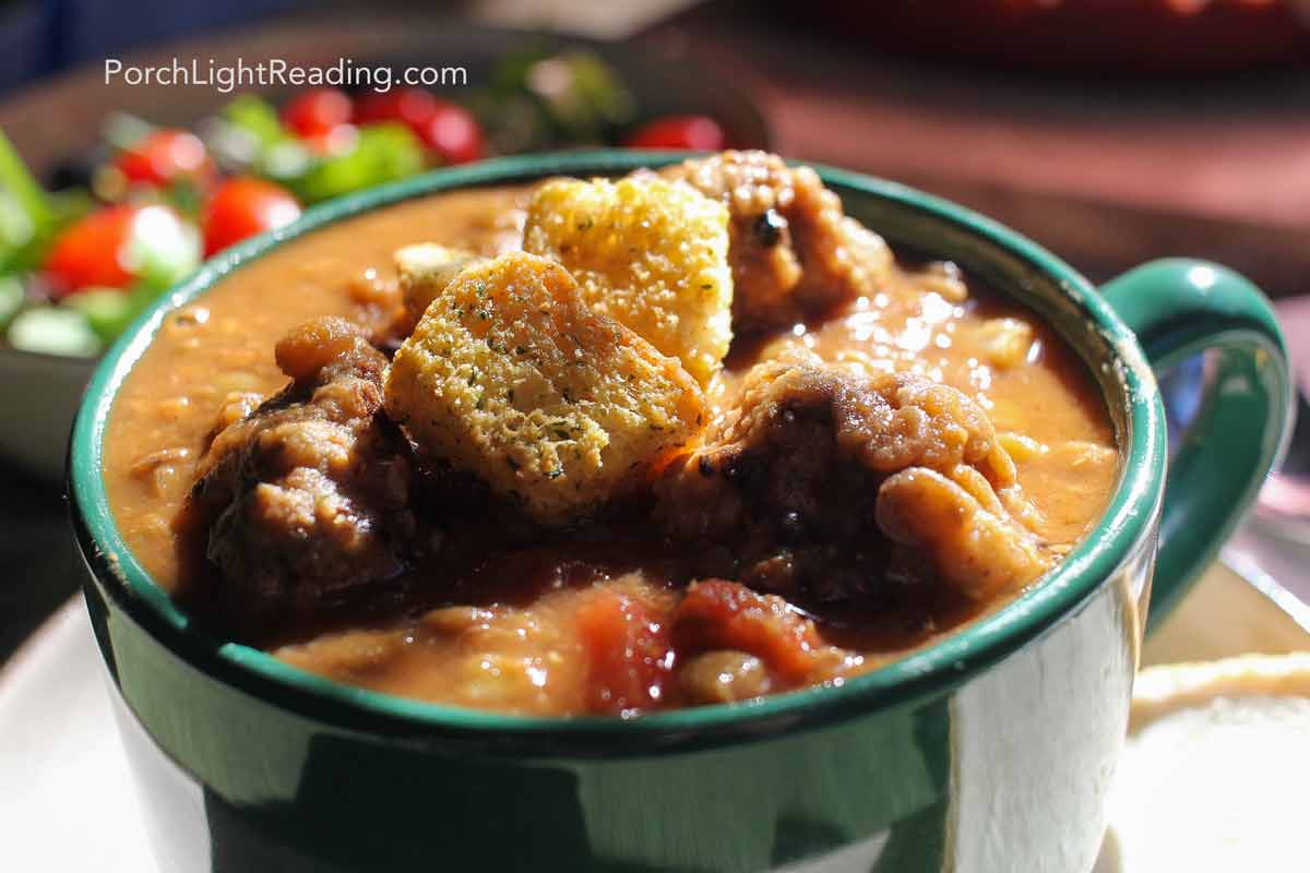 Green bowl of lentil meatball soup, served with a side salad. 