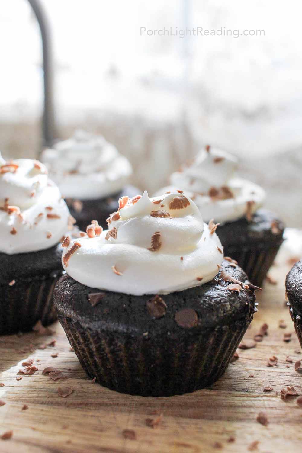 Chocolate black bean cupcakes on a wooden cutting board with topped with chocolate shavings. 