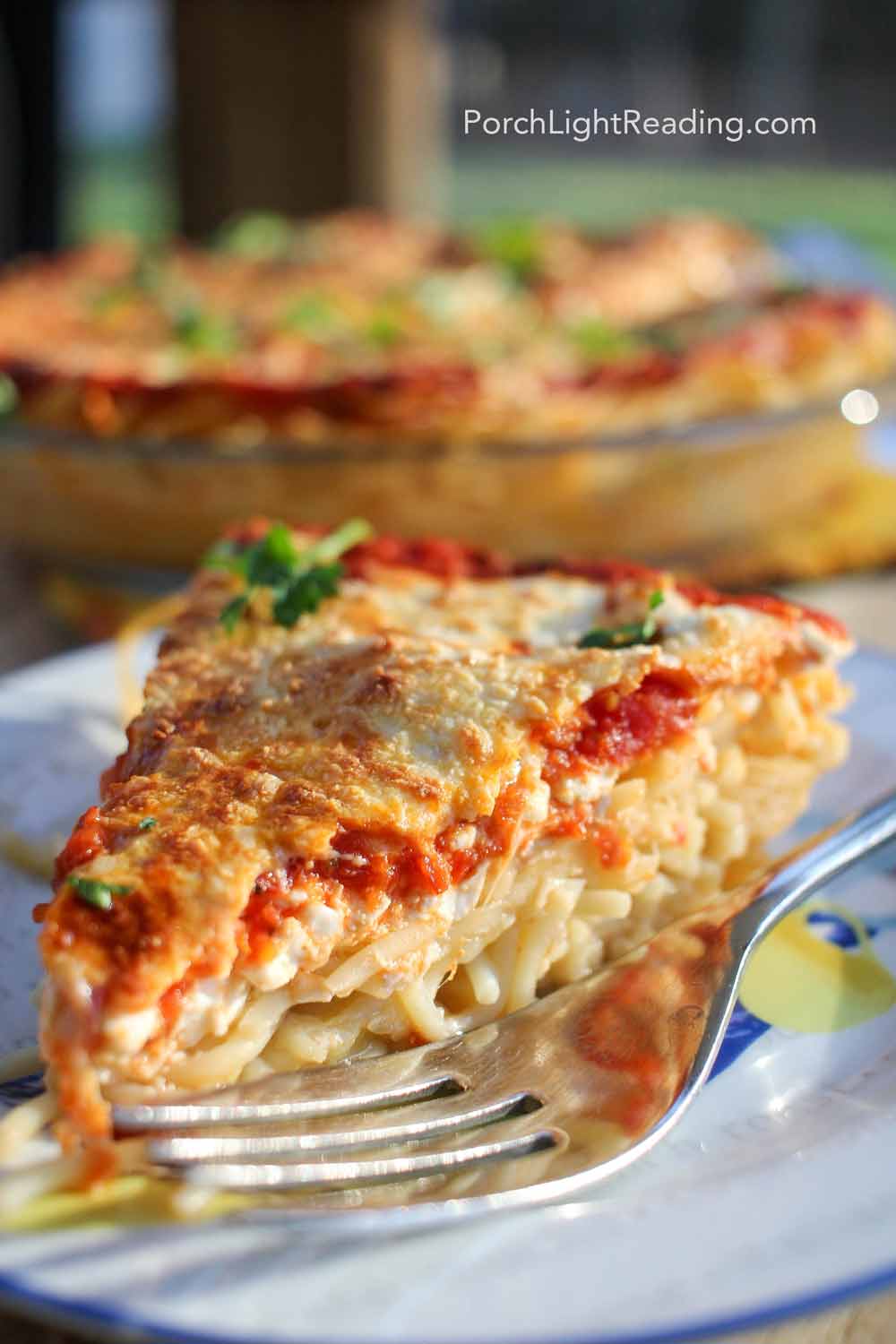 Spaghetti pie on a while plate with bubbly, golden mozzarella. 