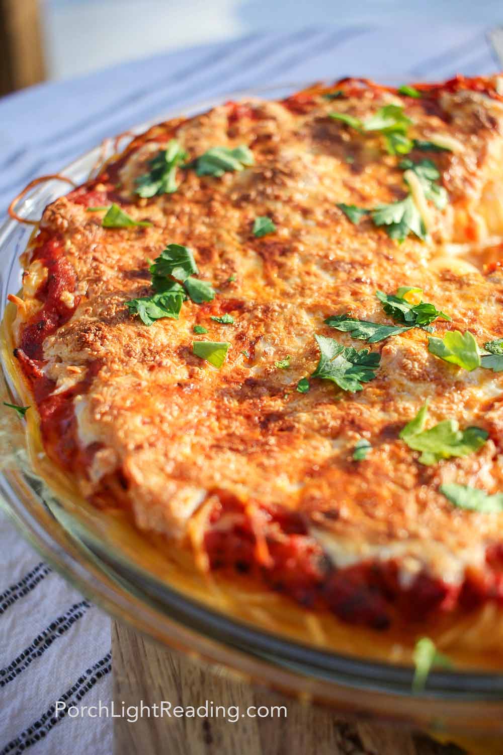 Spaghetti pie in a glass dish topped with golden cheese and fresh parsley. 