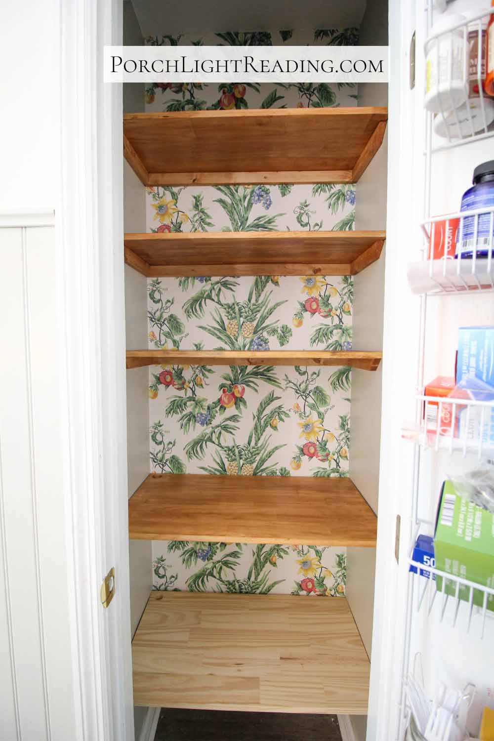 5 Wooden pantry shelves with tropical wallpaper behind them. 