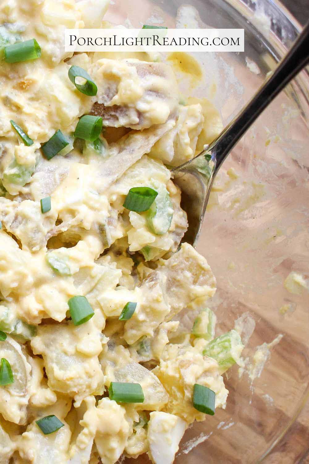 Potato salad in a glass serving dish and spoon for scooping. 