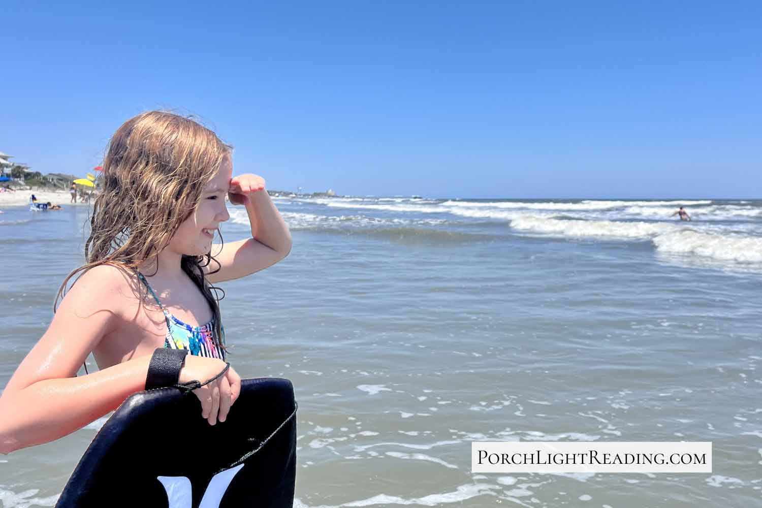 Little girl looking down the beach of Charleston, SC, with a boogie board. 