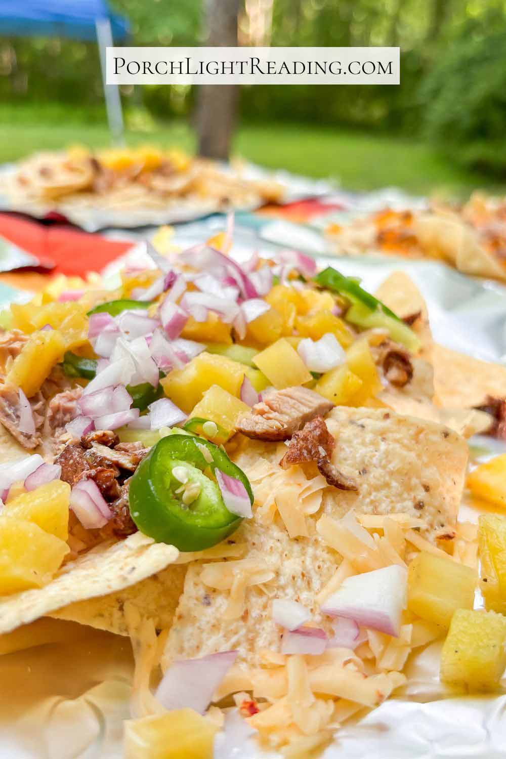 Tin foil nacho packets topped with pulled pork, pineapple, red onion, jalapeno, and cheese. 
