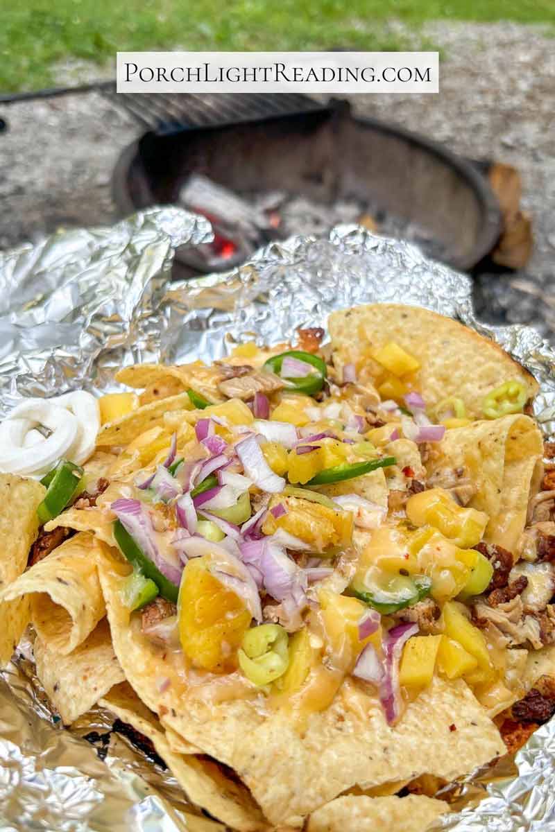 Campfire nachos with an open tin foil plate, sitting around the campfire. 