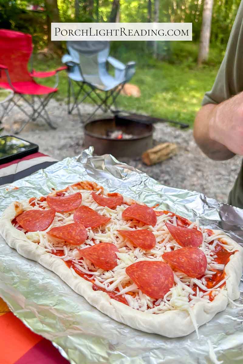 Prepping the campfire pizza by shaping the dough, adding sauce, cheese, and toppings. 