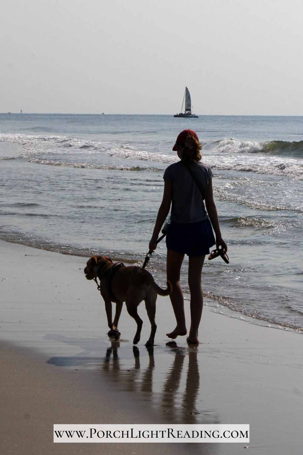 Young girl walking her dog along the beaches of Huntington Beach State Park. 