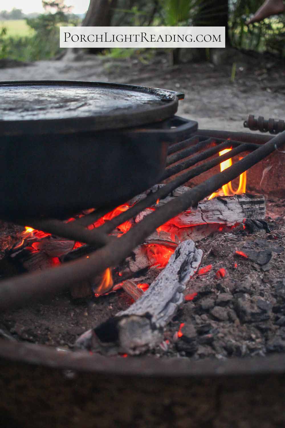 Hot coals under a campfire grate with a deep skillet for cooking.