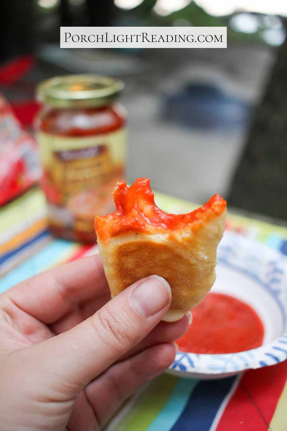 Golden pizza pocket dipped in pizza sauce, with a big bite taken out of it.