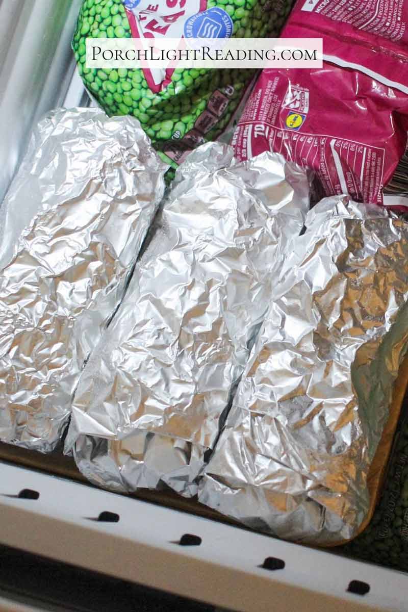 Breakfast burritos wrapped in tin foil in the freezer next to the peas.