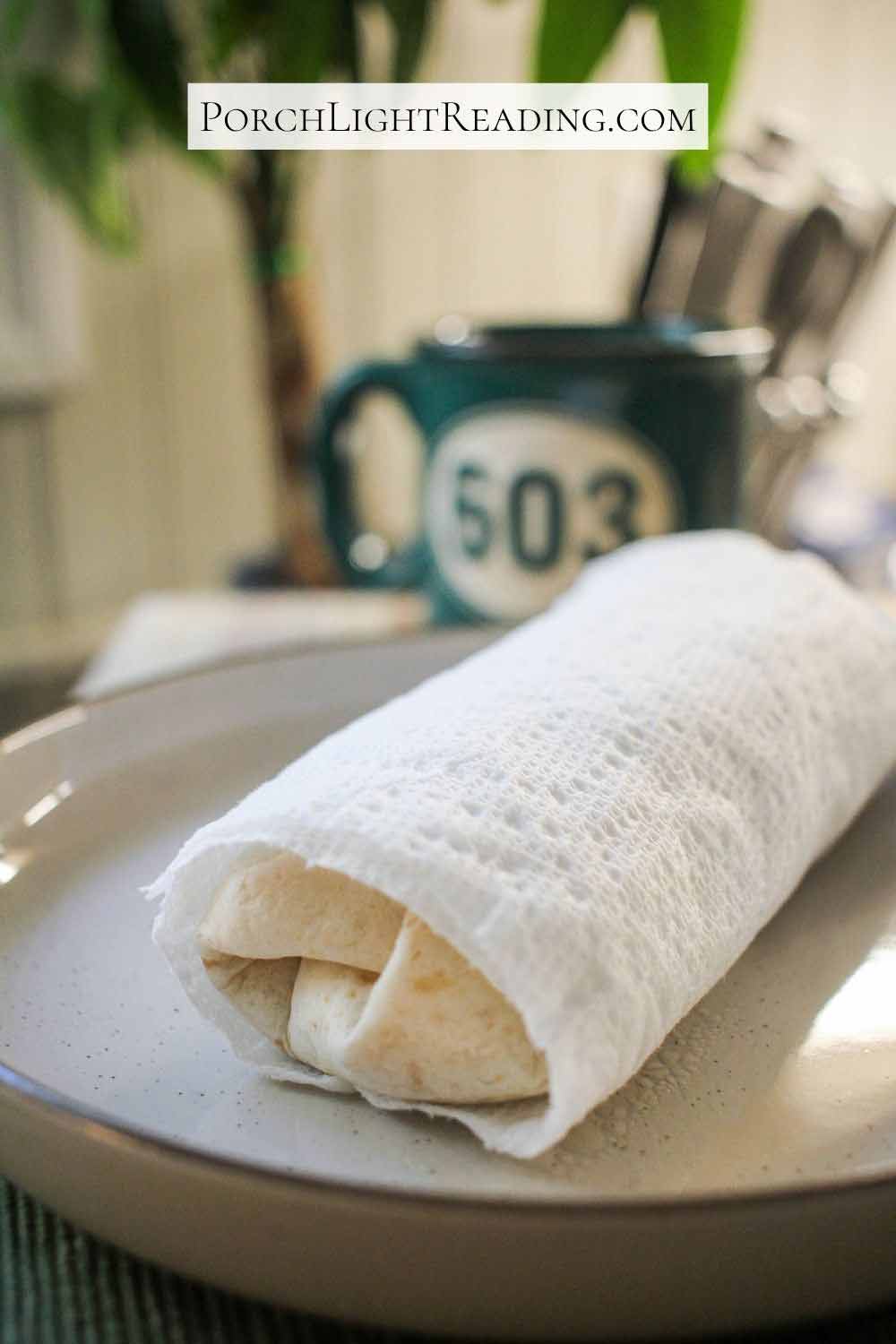 Breakfast burrito wrapped in a paper towel and ready to be microwaved.