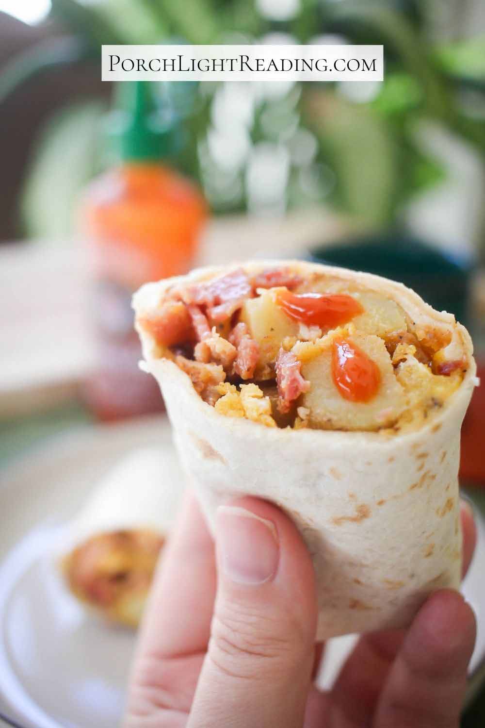 Showing the filling of a breakfast burrito and topped with hot sauce.
